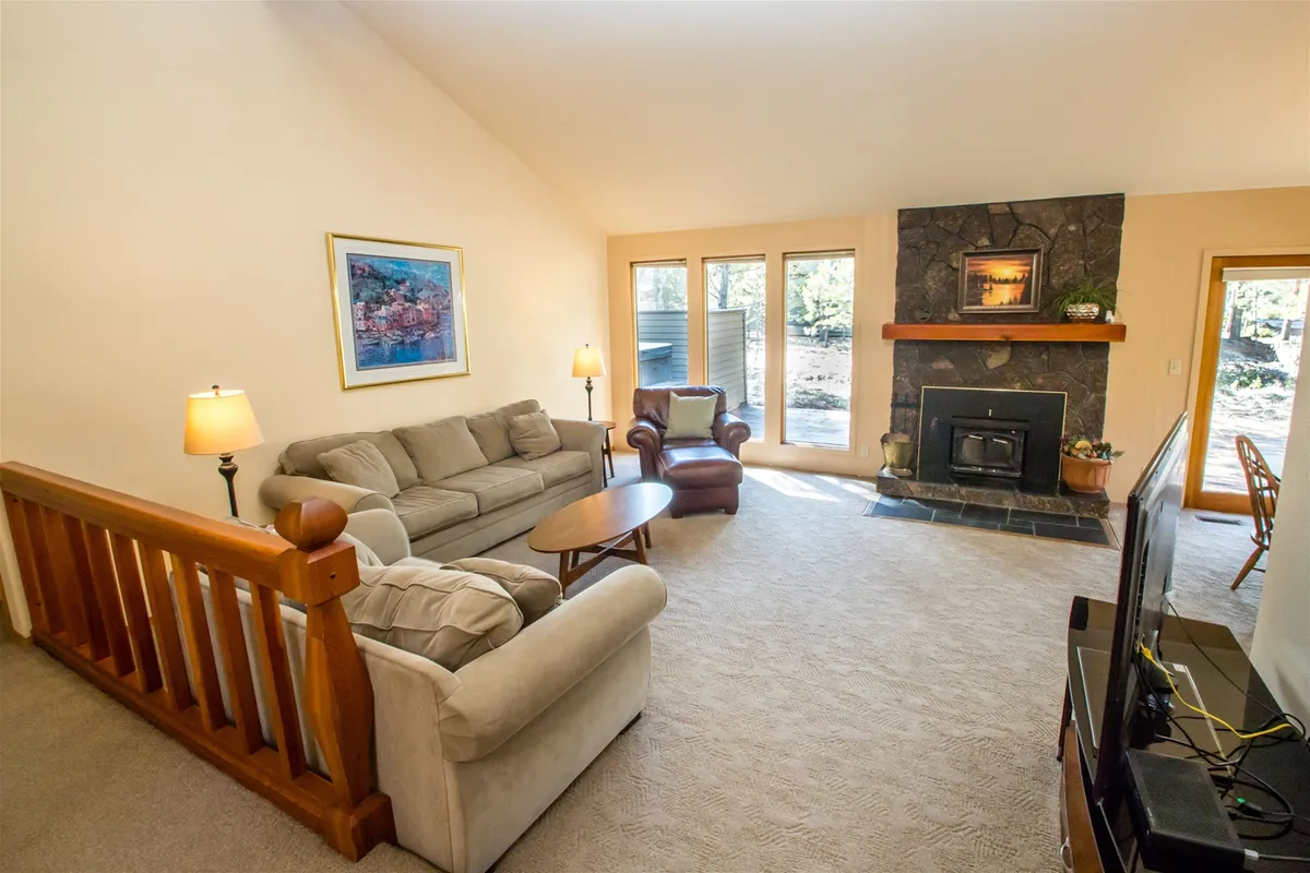 A welcoming living room featuring a plush sofa, a glowing fireplace, and expansive windows that flood the space with natural light. Artwork adorns the walls, adding personality and warmth to the open-concept area, while the layout encourages relaxation and togetherness.