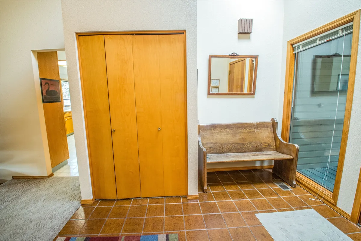 An entryway area with a wooden bench, mirror, closet doors, and a sliding glass door leading to the outside. The scene suggests accessibility to the outdoors and a practical space for gearing up or winding down after outdoor activities.