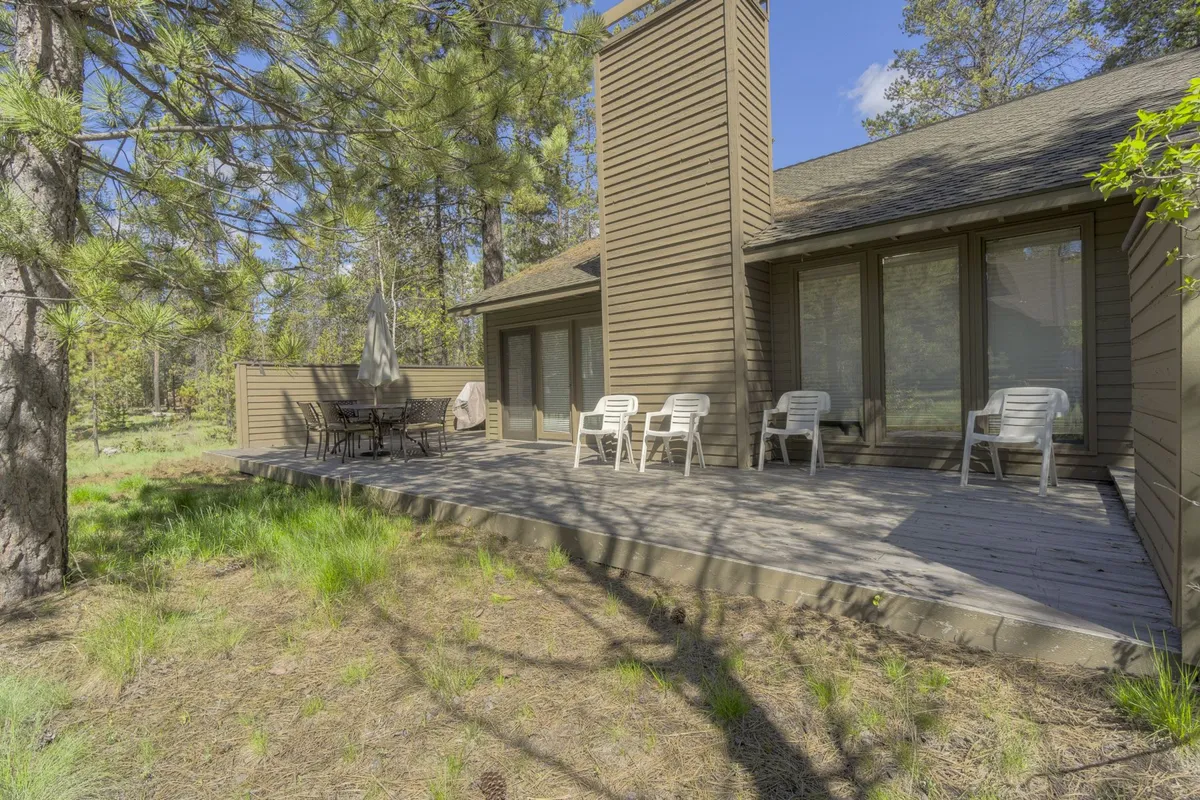 A spacious deck with chairs and a table, complemented by the silhouette of a chimney, invites outdoor dining and social gatherings while offering views of the surrounding wooded landscape.
