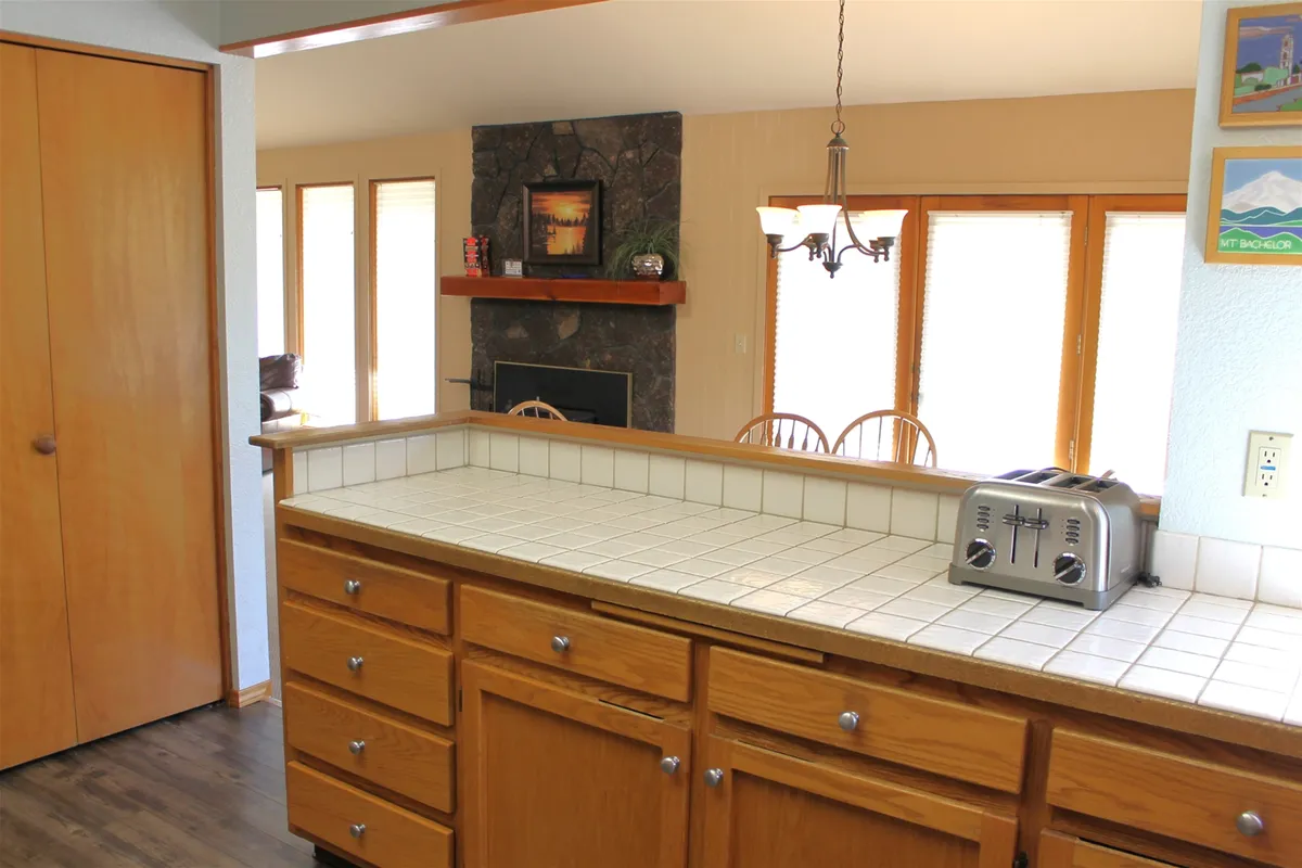 A wide-angle view of an open living area featuring a kitchen island, fireplace, and windows that let in ample natural light. The arrangement welcomes gatherings, meals, and cozy evenings in a bright, connected atmosphere.
