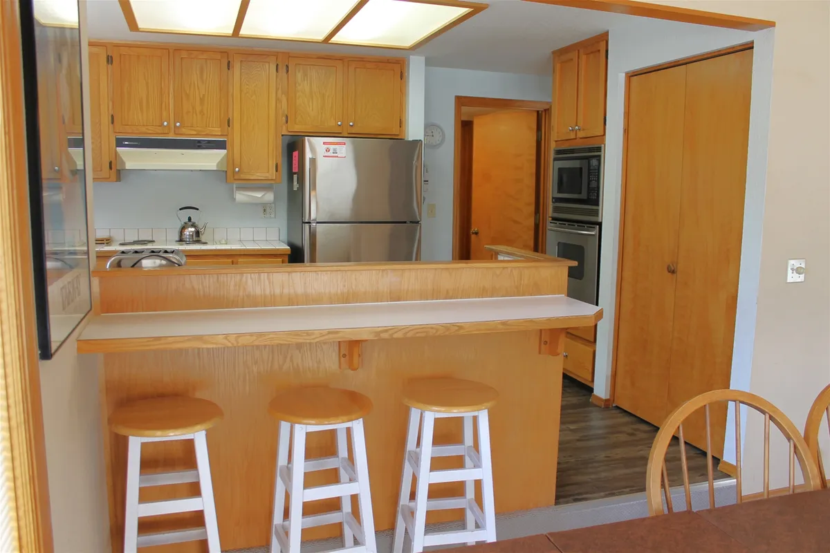 This image presents a kitchen island with stools, surrounded by visible appliances and warm wood cabinetry. The layout provides ample space for cooking, entertaining, and casual family meals, capturing the open-concept and social aspects of the kitchen.
