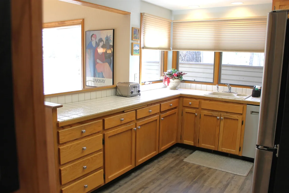 This image features a kitchen counter with a sink, a window that fills the space with natural light, and various small appliances visible, including a toaster. There is also some artwork on the wall, enhancing the modern and homey vibe. The setup showcases a portion of the kitchen workspace ideal for preparing meals and beverages.