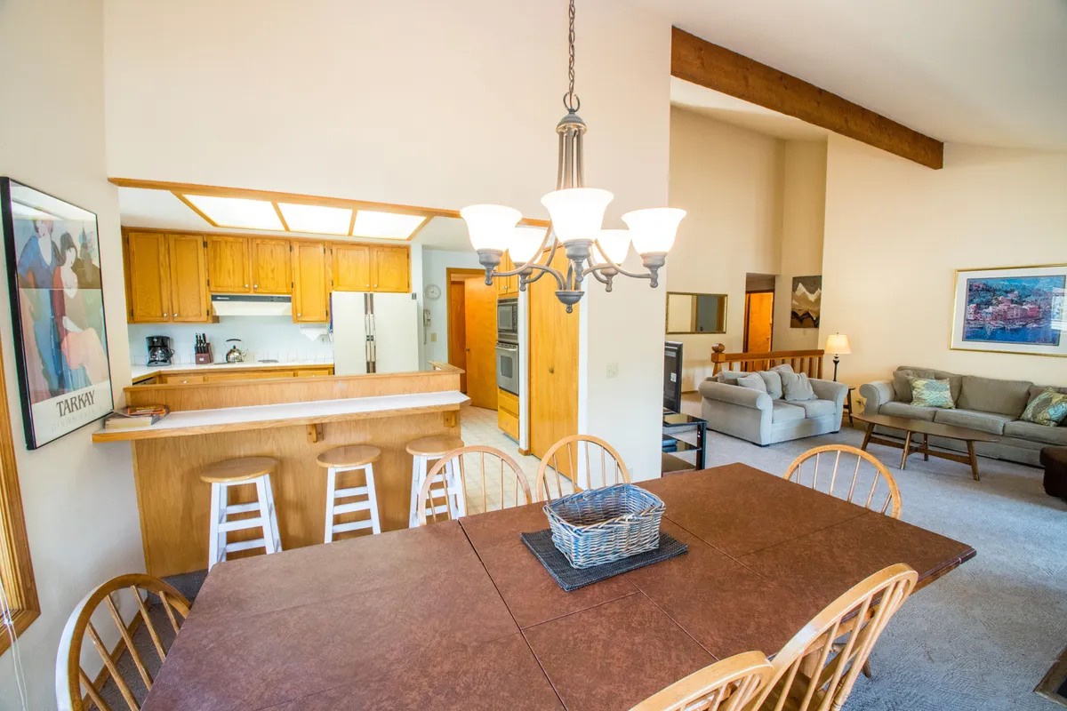 An open-concept area seamlessly combining a dining table under a stylish chandelier, a kitchen bar, and a comfortable couch zone. The space is designed for family meals, entertaining, and effortless flow between living and dining areas.